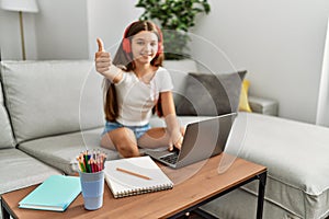 Young brunette teenager doing homework with laptop at home smiling happy and positive, thumb up doing excellent and approval sign