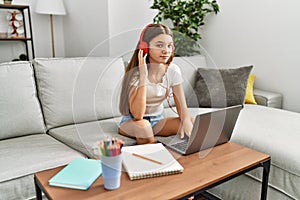 Young brunette teenager doing homework with laptop at home thinking attitude and sober expression looking self confident