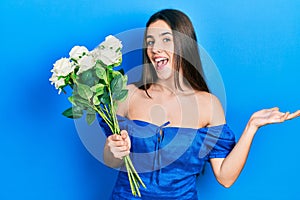 Young brunette teenager holding bouquet of white flowers celebrating achievement with happy smile and winner expression with