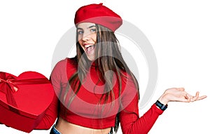 Young brunette teenager holding heart draw celebrating achievement with happy smile and winner expression with raised hand