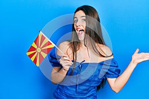 Young brunette teenager holding macedonian flag celebrating achievement with happy smile and winner expression with raised hand