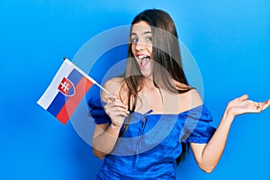 Young brunette teenager holding slovakia flag celebrating achievement with happy smile and winner expression with raised hand