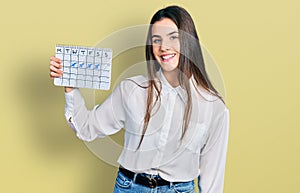 Young brunette teenager holding travel calendar looking positive and happy standing and smiling with a confident smile showing