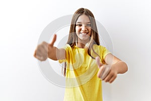 Young brunette teenager standing together over isolated background approving doing positive gesture with hand, thumbs up smiling