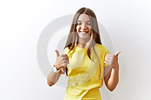 Young brunette teenager standing together over isolated background success sign doing positive gesture with hand, thumbs up
