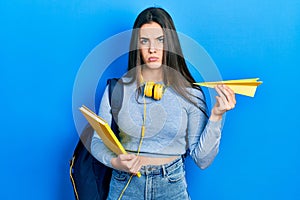 Young brunette teenager student holding books and paper plane depressed and worry for distress, crying angry and afraid