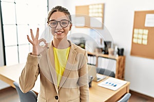 Young brunette teenager wearing business style at office smiling positive doing ok sign with hand and fingers