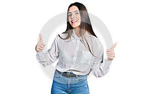 Young brunette teenager wearing business white shirt success sign doing positive gesture with hand, thumbs up smiling and happy
