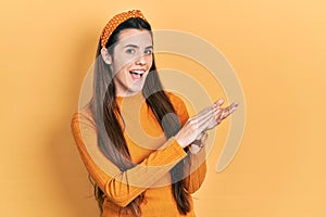 Young brunette teenager wearing casual yellow sweater clapping and applauding happy and joyful, smiling proud hands together