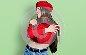 Young brunette teenager wearing french look with beret hugging oneself happy and positive, smiling confident