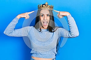Young brunette teenager wearing princess crown celebrating crazy and amazed for success with open eyes screaming excited
