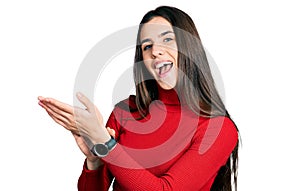 Young brunette teenager wearing red turtleneck sweater clapping and applauding happy and joyful, smiling proud hands together