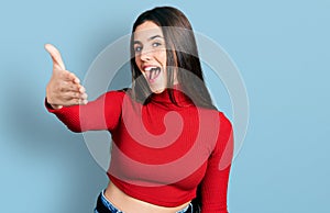 Young brunette teenager wearing red turtleneck sweater smiling friendly offering handshake as greeting and welcoming