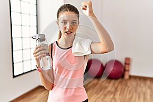 Young brunette teenager wearing sportswear holding water bottle angry and mad raising fist frustrated and furious while shouting