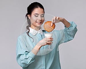 Young brunette wetting a cookie in a glass of milk