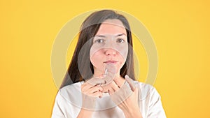 Young brunette who checks her skin on yellow background. Woman with problem skin applies medicine with a cotton swab