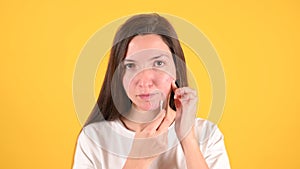 Young brunette who checks her skin on yellow background. Woman with problem skin applies medicine with a cotton swab