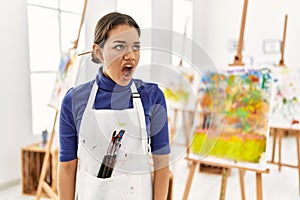 Young brunette woman at art studio angry and mad screaming frustrated and furious, shouting with anger