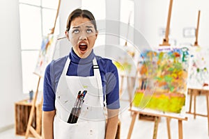 Young brunette woman at art studio angry and mad screaming frustrated and furious, shouting with anger