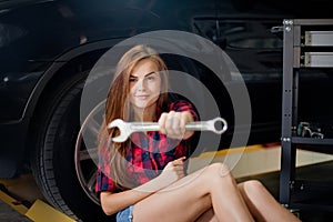 Young brunette woman as a mechanic in checked shirt show wrench. Blur macro