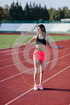 Young brunette woman athlete in pink shorts and black top on stadium sporty lifestyle standing on track holding jump rope under