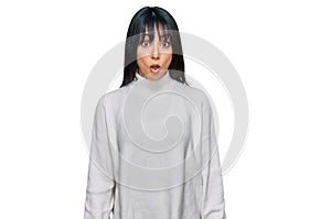 Young brunette woman with bangs wearing casual turtleneck sweater afraid and shocked with surprise expression, fear and excited