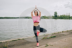 Young brunette woman with bare feet  wearing black and purple fitness outfit  stretching on violet yoga mat outside on wooden pier photo