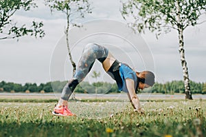 Young brunette woman with bare feet  wearing black and purple fitness outfit  stretching on violet yoga mat outside on wooden pier photo