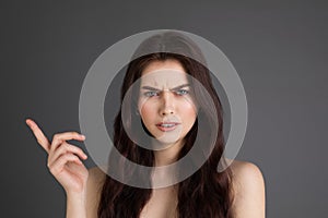 Young brunette woman with bare shoulders smirking from disbelief frowning while pointing at apper left corner