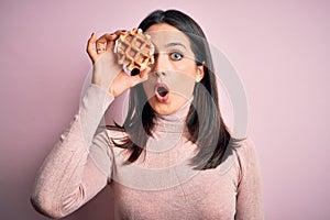 Young brunette woman with blue eyes eating sweet waffle for breakfast over white background scared in shock with a surprise face,