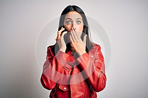 Young brunette woman with blue eyes having a conversation talking on smartphone cover mouth with hand shocked with shame for