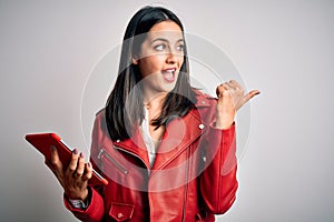 Young brunette woman with blue eyes using touchpad tablet over  background pointing and showing with thumb up to the side