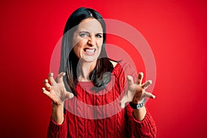 Young brunette woman with blue eyes wearing casual sweater over isolated red background smiling funny doing claw gesture as cat,