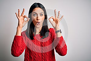 Young brunette woman with blue eyes wearing casual sweater over isolated white background looking surprised and shocked doing ok