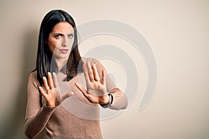 Young brunette woman with blue eyes wearing casual sweater over isolated white background Moving away hands palms showing refusal