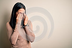 Young brunette woman with blue eyes wearing casual sweater over  white background rubbing eyes for fatigue and headache,