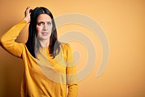 Young brunette woman with blue eyes wearing casual sweater over yellow background confuse and wonder about question