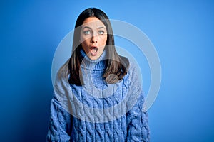 Young brunette woman with blue eyes wearing casual turtleneck sweater afraid and shocked with surprise and amazed expression, fear