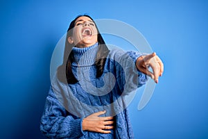 Young brunette woman with blue eyes wearing casual turtleneck sweater laughing at you, pointing finger to the camera with hand