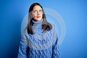 Young brunette woman with blue eyes wearing casual turtleneck sweater smiling looking to the side and staring away thinking