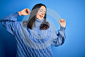 Young brunette woman with blue eyes wearing casual turtleneck sweater stretching back, tired and relaxed, sleepy and yawning for