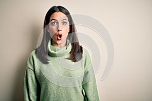 Young brunette woman with blue eyes wearing turtleneck sweater over white background afraid and shocked with surprise expression,