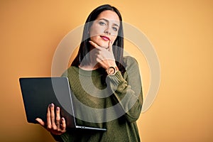 Young brunette woman with blue eyes working using computer laptop over yellow background looking confident at the camera smiling