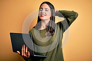 Young brunette woman with blue eyes working using computer laptop over yellow background smiling confident touching hair with hand