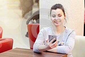 Young brunette woman in cafe uses smartphone and smiles. The girl is in the wi fi wi-fi zone of the cafe