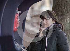 Young brunette woman calling from a red street payphone, looking directly at the camera