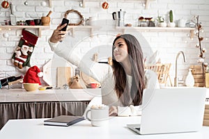 Young brunette woman chatting with friends using her mobile phone at the kitchen