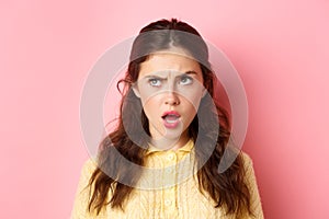 Young brunette woman with confused face, trying figure something out, frowning and looking up while thinking, standing