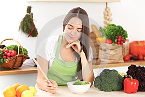 Young brunette woman is cooking or eating fresh salad in the kitchen. Housewife holding wooden spoon in her right hand