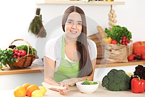 Young brunette woman is cooking or eating fresh salad in the kitchen. Housewife holding wooden spoon in her right hand